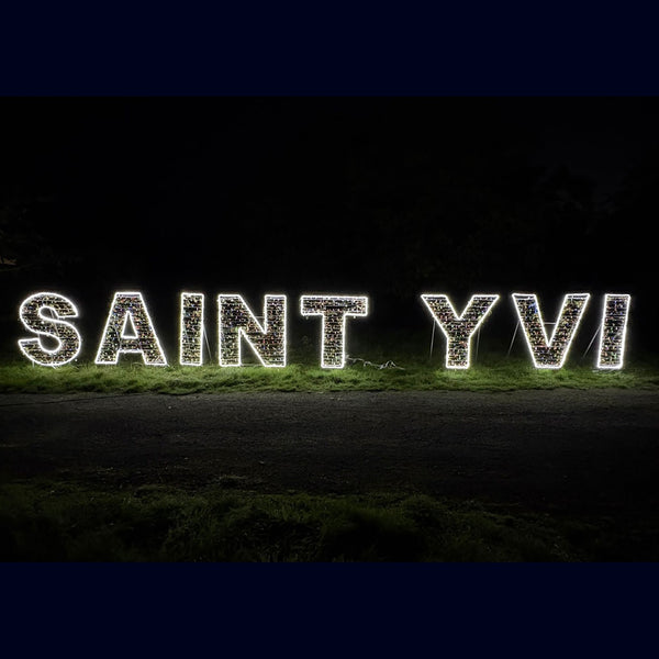Lettres lumineuses formant le nom d’une commune, posées sur une pelouse, de nuit